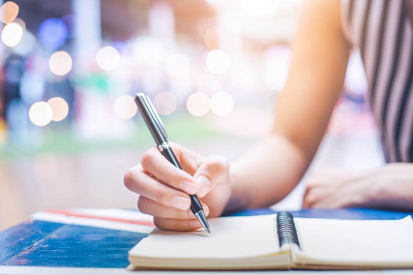 Intern. International student. Woman's hand writing on a notebook with a pen on a wooden desk.