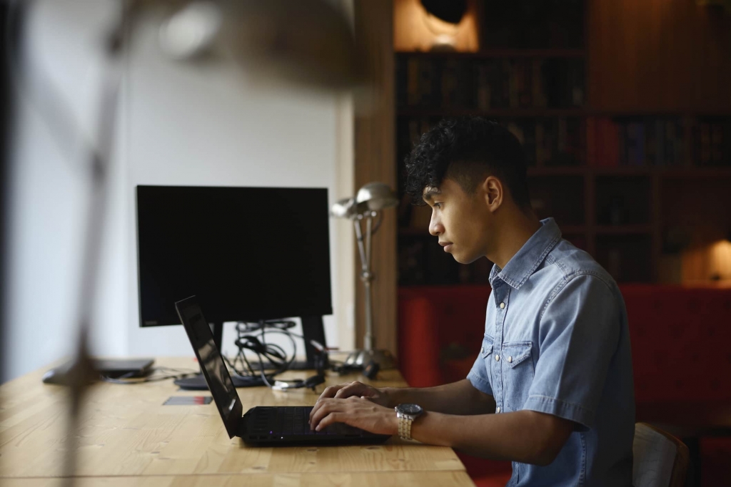 한 남자가 책상에 앉아 노트북으로 작업하고 있다.