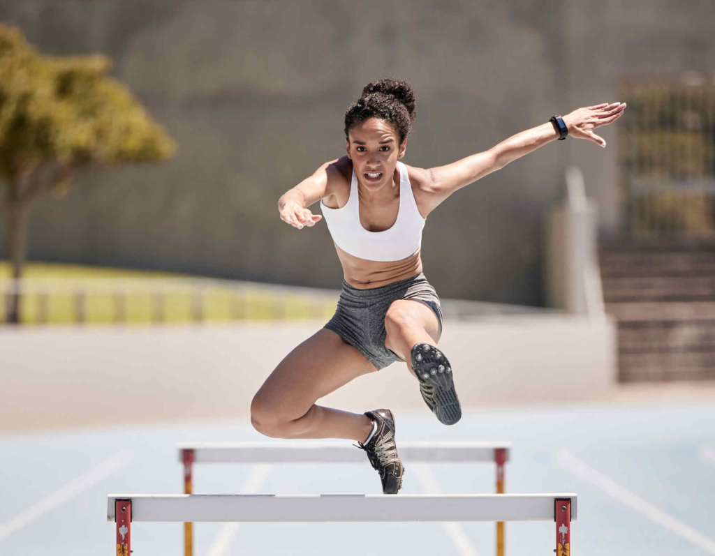 A female athlete in athletic gear is practicing her hurdling technique on a track.